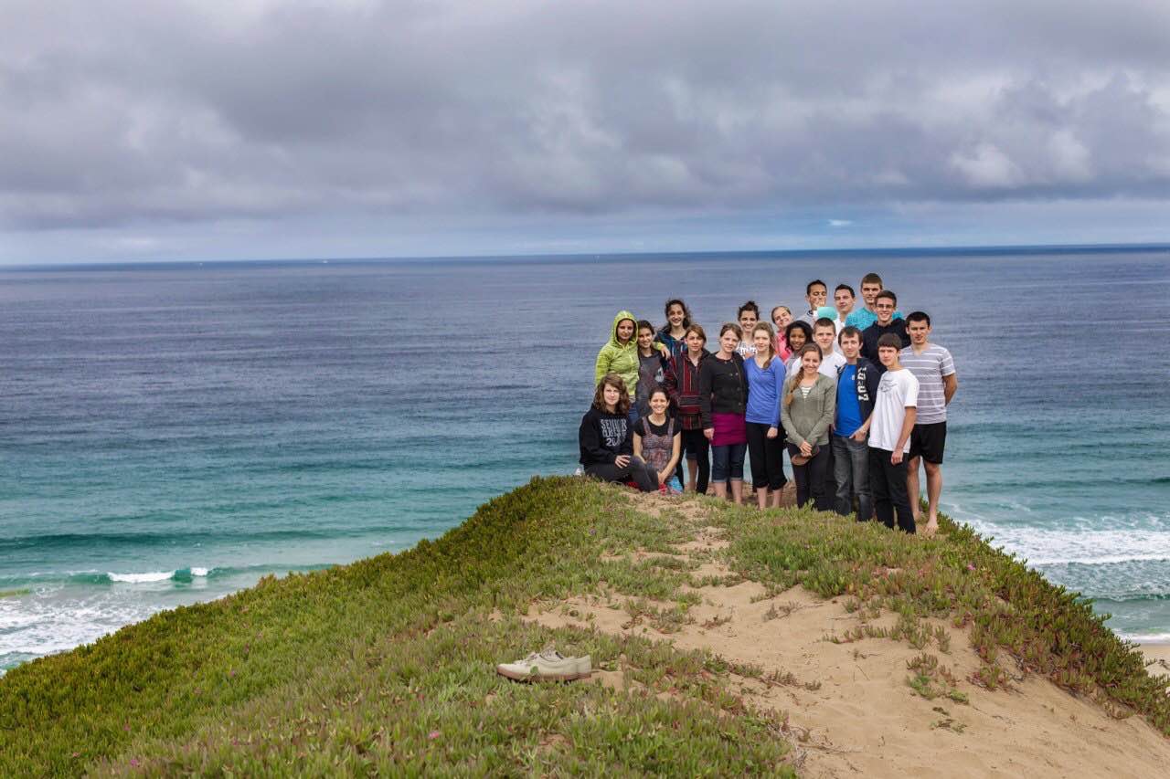 Group stand on the edge of a cliff in front of the ocean.