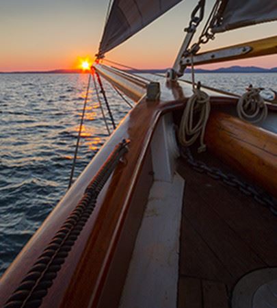 Bow of a sailboat on the water with sunset in the background